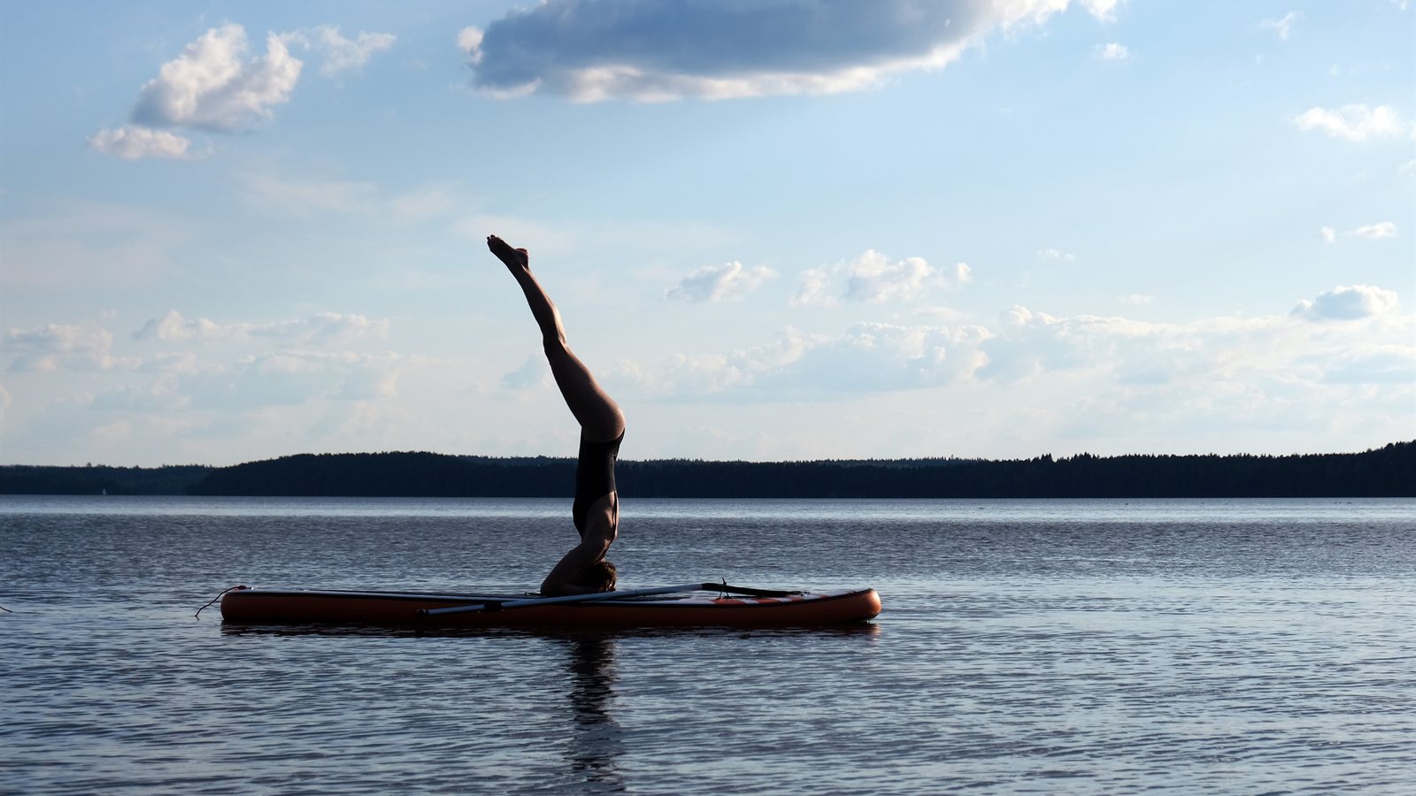 Person doing a headstand on a paddleboard in still water