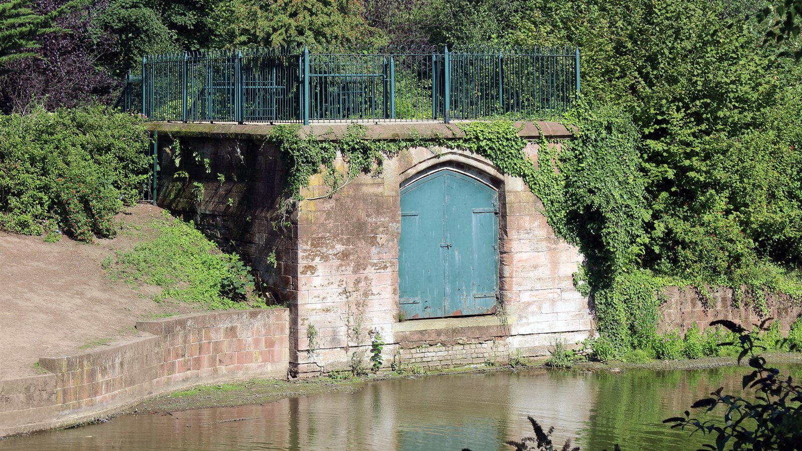 Old stone boathouse with blue doors beside still green water